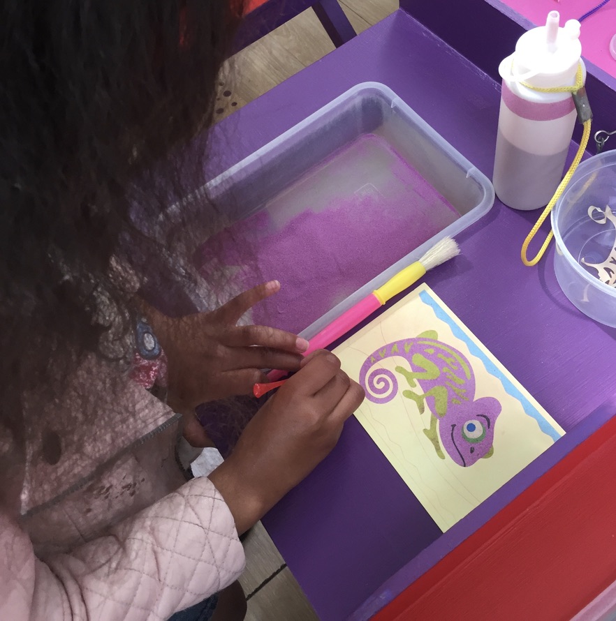 A child pours coral coloured sand onto a patterned card design